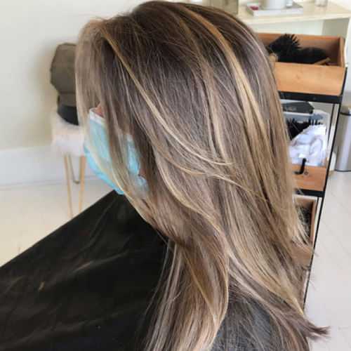 Person with layered, ash blonde hair, wearing a blue mask, sitting in a salon.