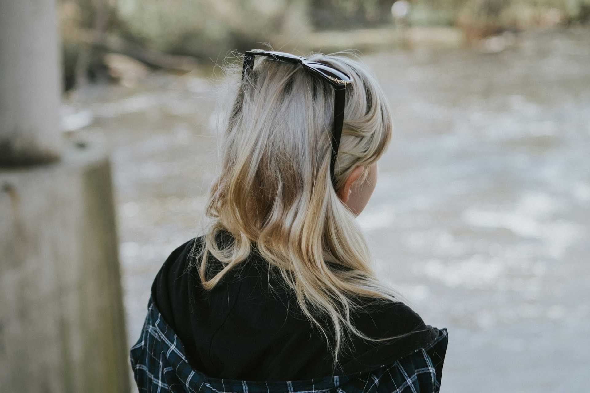 Blonde woman with sunglasses on head, looking at riverside scenery.
